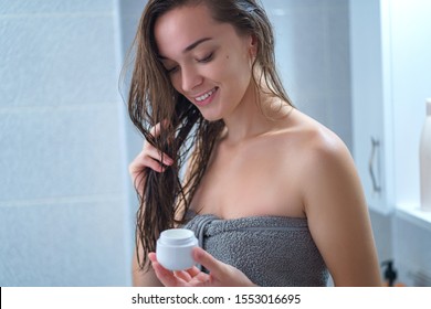 Happy Attractive Young Woman In Bath Towel Apply Moisturizing Conditioner To Hair In Bathroom After Shower At Home. Hair Care And Hydration, Female Care. Healthy Hair 