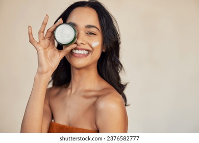 Happy attractive young woman hold green cream jar and covering eye while looking at camera with a big laugh. Portrait of multiethnic beauty woman with organic and herbal cream for healthy skin. - Powered by Shutterstock