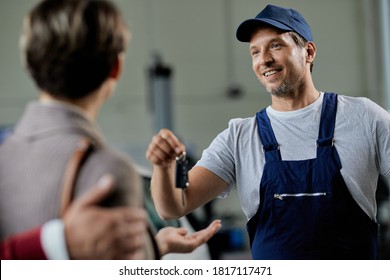 Happy auto repairman handing over cark keys to his customers in a workshop.  - Powered by Shutterstock