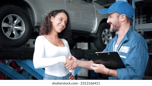 Happy automotive mechanic man in uniform shaking hands with women client at auto repair shop. Car service, repair, maintenance, gestures and man-mechanic concept - Powered by Shutterstock