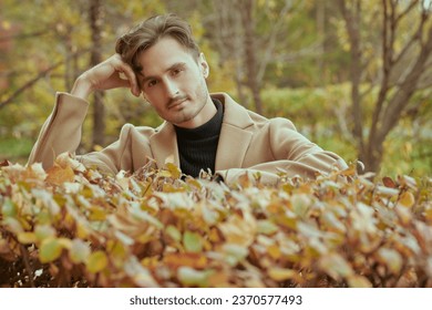 Happy autumn day. A handsome young man in a brown coat stands in an autumn park and smiles peacefully. Autumn fashion. People and lifestyle. Copy space. - Powered by Shutterstock