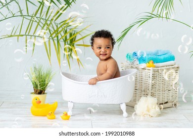 A happy baby African taking a bath, playing with foam bubbles and a duck toy. Infant washing and bathing. Hygiene and caring for young children
