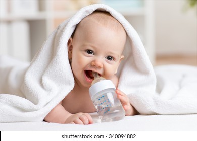 Счастливый мальчик пьет воду из обернутого бутылочкой полотенца после ванны