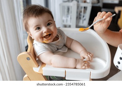 Happy baby boy eating first food pumpkin from spoon with mom at home - Powered by Shutterstock