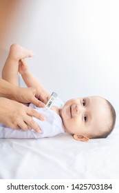 Happy baby boy feeling well after the illness. Young mother using thermometer to take baby's temperature underarm. A thermometer showing the normal range of kid's temperature. Family health concept.