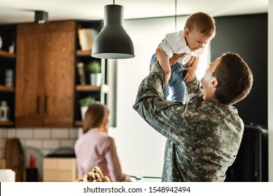 Happy baby boy having fun with his military dad at home. Mother is in the background. 