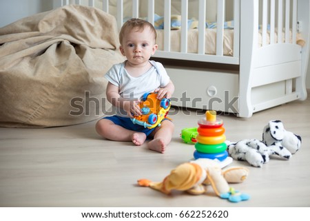 Happy baby boy playing with toys on floor at bedroom