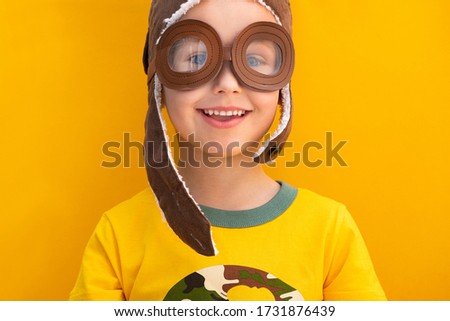 Happy baby boy in retro pilot's helmet play on a yellow background.