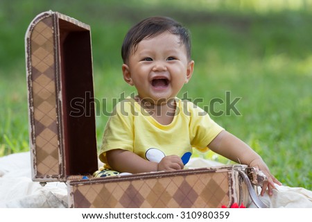 happy baby boy in yellow shirt sit in brown luggage outdoor