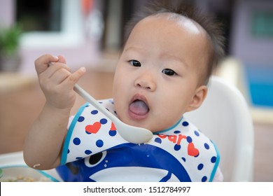 Happy Baby Child Sitting In Chair With A Spoon.Children Eat By Themselves.