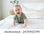 Happy baby. Cute little newborn girl with smiling face crawling on bed in bedroom. Infant baby resting playing lying down on blanket at home. Motherhood happy child childcare concept
