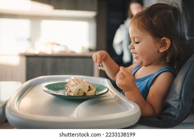 Happy baby girl looking at the tasty dessert on her plate. The child enjoy self eating meal sweet fruit and laughing happiness. Baby healthcare and nutrition