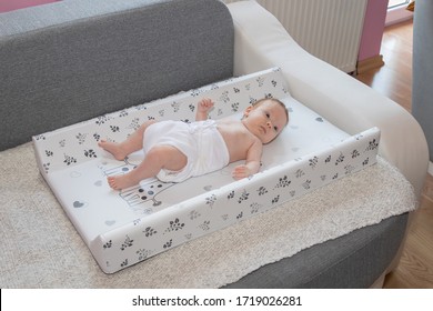 Happy Baby Girl Lying On Diaper Changing Pad, Wearing A Diaper. Cute Adorable Baby Is 3 Months Old. Dry And Healthy Body And Skin For Children Concept. 