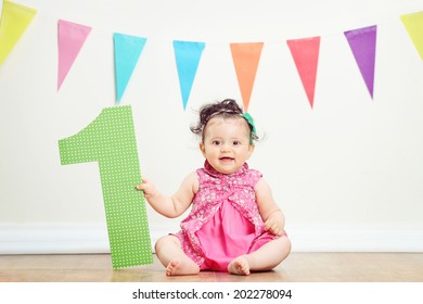 Happy baby girl on her first birthday party seated on the floor