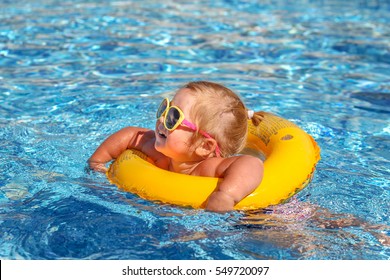 Happy Baby Girl Playing In Pool On A Hot Summer Day During Vacation