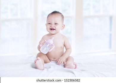 Happy baby holding a bottle at home