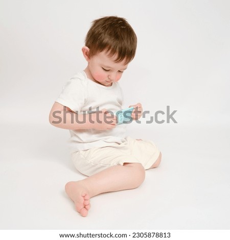 Happy baby holding a tube of cream on a studio white background. Smiling child plays with a package of ointment. Kid about two years old (one year nine months)