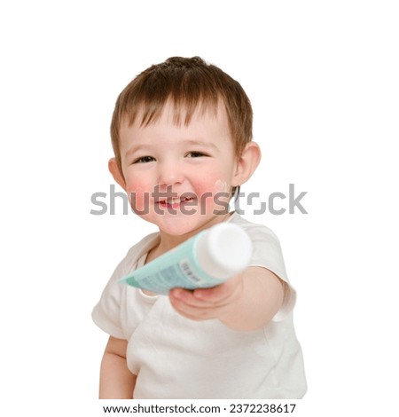 Happy baby holding a tube of cream on a studio, isolated on white background. Smiling child plays with a package of ointment. Kid about two years old (one year nine months)