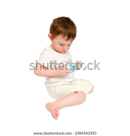 Happy baby holding a tube of cream on a studio, isolated on white background. Smiling child plays with a package of ointment. Kid about two years old (one year nine months)