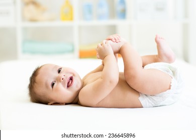 happy baby lying on white sheet and holding his legs