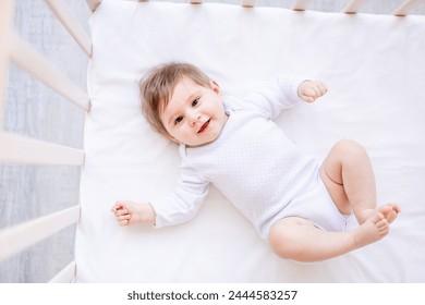 bebé recién nacido feliz en una cuna blanca en un dormitorio brillante primer plano en ropa blanca sonriendo o riendo, lugar para texto, vista superior.