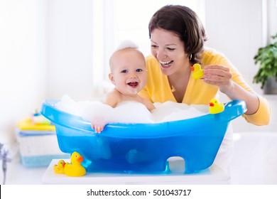 Happy Baby Taking A Bath Playing With Foam Bubbles. Mother Washing Little Boy. Young Child In A Bathtub. Smiling Kids In Bathroom With Toy Duck. Mom Bathing Infant. Parent And Kid Play With Water.