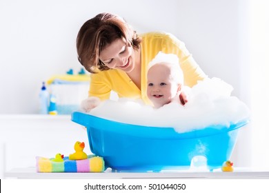 Happy Baby Taking A Bath Playing With Foam Bubbles. Mother Washing Little Boy. Young Child In A Bathtub. Smiling Kids In Bathroom With Toy Duck. Mom Bathing Infant. Parent And Kid Play With Water.