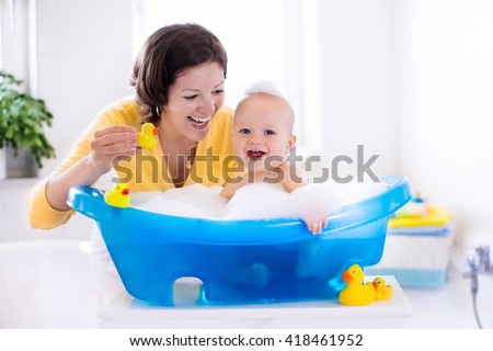 Happy baby taking a bath playing with foam bubbles. Mother washing little boy. Young child in a bathtub. Smiling kids in bathroom with toy duck. Mom bathing infant. Parent and kid play with water.