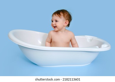 Happy Baby Toddler Boy Is Sitting In A White Tub On A Studio Blue Background. A Smiling Child At The Age Of One Year, Copy Space