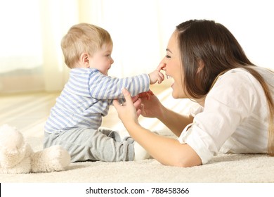 Happy baby touching his mother face lying on a carpet at home