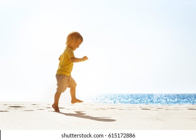 Happy baby walking ot jumping at white lonely beach on blue sea background