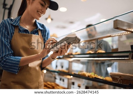 Happy bakery shop worker using credit card reader while serving her customer. 