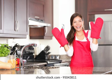 Happy Baking Cooking Woman Standing In Her New Kitchen Smiling Cheerful Wearing Apron And Oven Mitts Ready To Bake. Beautiful Young Mixed Race Caucasian / Chinese Woman At Home.