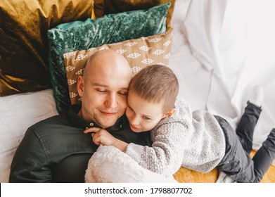 Happy Bald Father And His Son Relaxing, Lying In Bed Together, Family Having Fun, Hugging And Cuddling, Smiling Dad And Child Boy Spending Weekend At Home. Warm Relationship. Closeup.