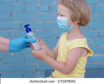 Happy Bald Mother In Green Dress, Medical Mask And Blue Gloves Holds Bottle With Disinfectant In Her Hands. Woman Teaches Her Child To Use Sanitizer For Reliable Protection Against Viruses