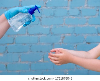 Happy Bald Mother In Green Dress, Medical Mask And Blue Gloves Holds Bottle With Disinfectant In Her Hands. Woman Teaches Her Child To Use Sanitizer For Reliable Protection Against Viruses