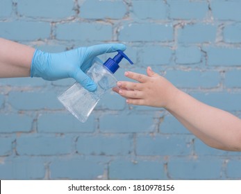 Happy Bald Mother In Green Dress, Medical Mask And Blue Gloves Holds Bottle With Disinfectant In Her Hands. Woman Teaches Her Child To Use Sanitizer For Reliable Protection Against Viruses