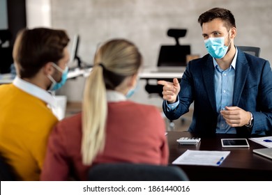 Happy Bank Manager Wearing Protective Face Mask While Consulting A Couple During A Meeting In The Office.