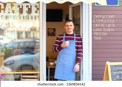 Happy barista standing at cafe entrance – portrait of mature business man attend new customers in her coffee shop – happy male owner holding cup of take-away cofee - Powered by Shutterstock