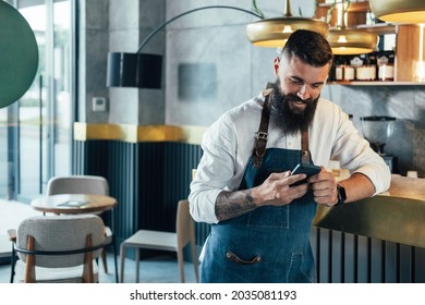 Happy Barista Using Mobile Phone in a Cafe.

Cheerful smiling waiter with a beard leaning on the bar counter and typing text message on his smartphone while working at the coffee shop.  - Powered by Shutterstock