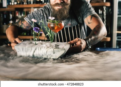 Happy barman is making cocktail with ice vapor at night club. Unique man. Bartender has a mustache and stylish hairstyle