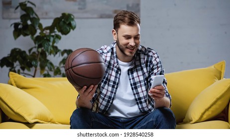 Happy Basketball Fan Holding Ball And Watching Match On Smartphone 