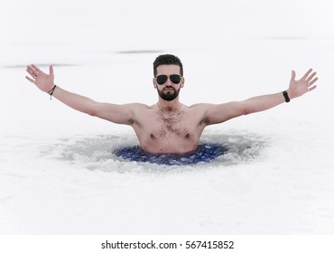happy bather with outstretched arms standing in a hole dug in the ice frozen lake