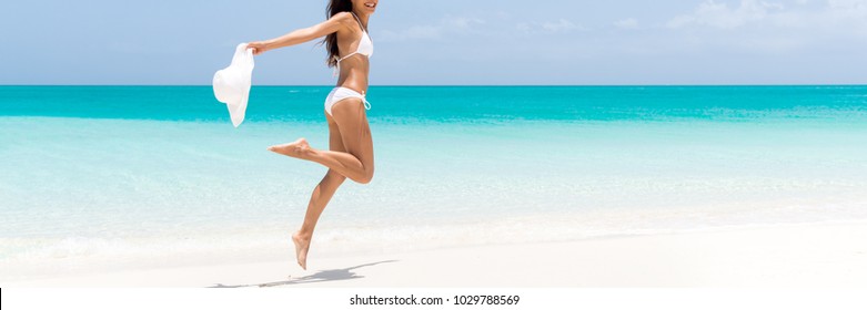 Happy beach body woman jumping of joy with sun hat on caribbean travel vacation. Slim legs sexy bikini girl sun tanning feeling free. Banner panorama with copy space on blue ocean background