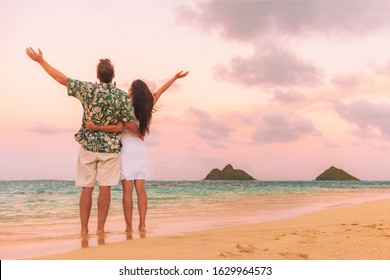 Happy Beach Vacation Couple Tourists Enjoying Sunset With Arms Up In Freedom View From Behind. Woman And Man Standing In Hawaiian Shirt Against Ocean Background Dusk In Lanikai, Oahu, Hawaii.