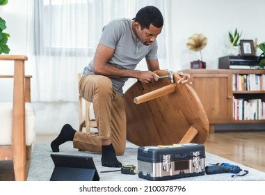 Happy Bearded African American Man Watching Online Tutorial Instructions For Assembling Furniture About Repairing Of Wooden Table. Black Man Looking On Digital Tablet Screen And Hammer Assembling.