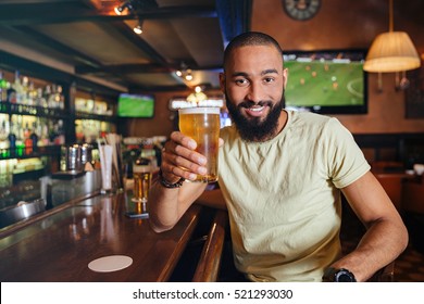 Happy Bearded African American Young Man Sitting And Drinking Beer In Bar 