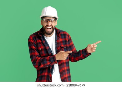 Happy Bearded Engineer Or Constructor Man In Casual Outfit Pointing Finger Away Over Green Background.