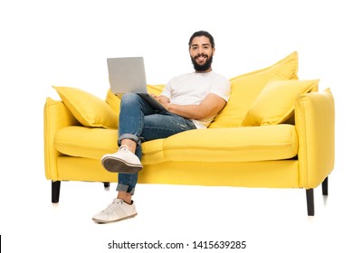 Happy Bearded Latin Man Using Laptop While Sitting On Yellow Sofa Isolated On White