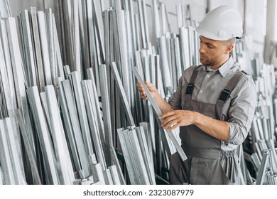 Happy bearded male factory worker in special uniform and white hard hat holding aluminum frame at production of metal plastic windows and doors - Powered by Shutterstock